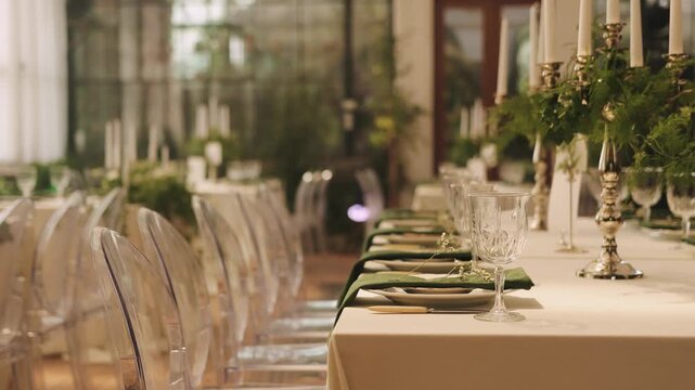 Wedding table setting with white linens, green napkins, glassware and greenery for a reception.