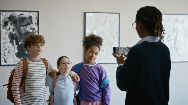 Over shoulder shot of African American male teacher taking photo of diverse school children posing in art gallery. Video is perfect for school marketing and field trip promotions
