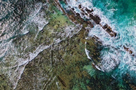 Aerial downward view of ocean waves crashing over the rugged rocky coastline at Brooms Head, capturing white surf, exposed rock formations and surrounding Pacific Ocean along the Clarence Valley coast