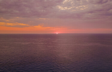 Fototapeta premium Aerial view of vibrant purple and orange sunset over quiet open Ionian sea horizon with dramatic cloudy sky in Lefkada island Greece horizontal stock photo