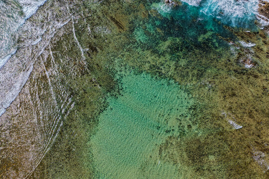 Aerial downward view of ocean waves crashing over the rugged rocky coastline at Brooms Head, capturing white surf, exposed rock formations and surrounding Pacific Ocean along the Clarence Valley coast