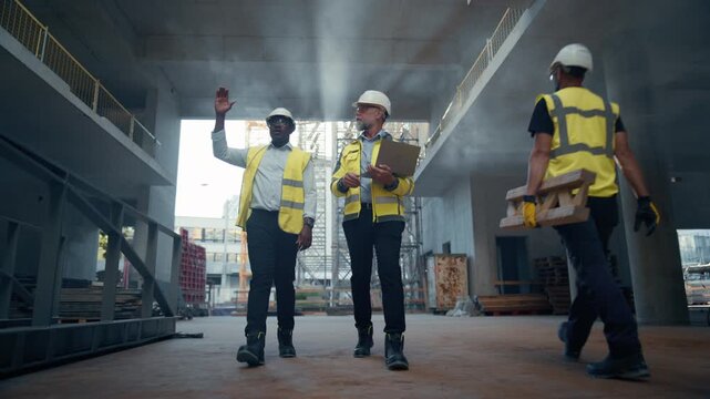 Real Estate Building Construction Site: Engineer and Architect Walk Through Future Data Center, Discussing Development Progress, While Using Laptop Computer. Cinematic Tracking Low Angle Shot