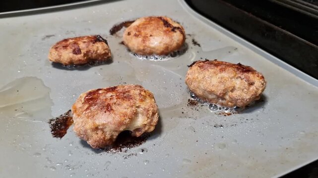 Seared burger patties sizzling on oiled tray in oven heat