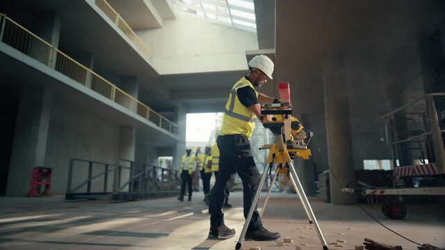 Real Estate Building Construction Site: Skilled Carpenter Cuts Wooden Plank With Miter Saw While Two Developers Walk in Background, Discussing Project Using Laptop Computer. Slow Motion Tracking Shot