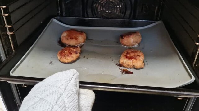 Hand in mitt pulling tray with browned patties from oven