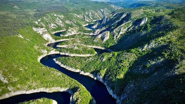 Aerial view of the dramatic meanders of the Uvac River Canyon in Serbia. Deep blue water winds in tight S-curves through steep limestone cliffs, lush green hills, and forested mountain terrain 