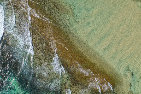Aerial downward view of ocean waves crashing over the rugged rocky coastline at Brooms Head, capturing white surf, exposed rock formations and surrounding Pacific Ocean along the Clarence Valley coast