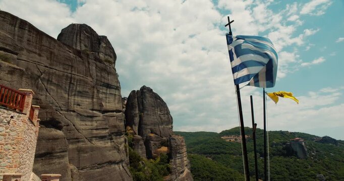A view of the rounded boulders Meteora rock formations in Thesally Greece with the greek and Greek Orthodox Church flag waving in the wind