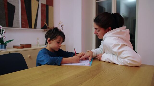 Mother supervises her child completing home study at the dining table at night, promoting independent learning, steady attention and responsible educational habits