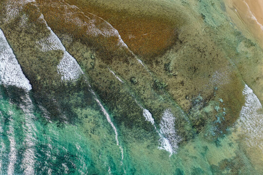 Aerial downward view of ocean waves crashing over the rugged rocky coastline at Brooms Head, capturing white surf, exposed rock formations and surrounding Pacific Ocean along the Clarence Valley coast