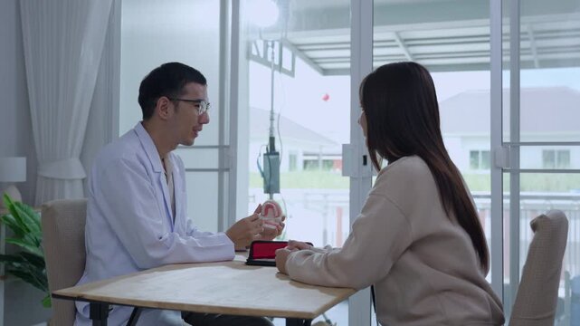 Asian male dentist holding a teeth model explaining oral care to a female doctor during a medical podcast interview. Recording a dental healthcare audio broadcast in a modern clinic studio.