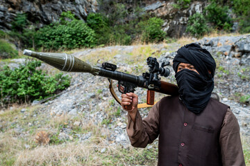 Naklejka premium Warrior holds a rocket launcher while standing in a rocky area surrounded by greenery