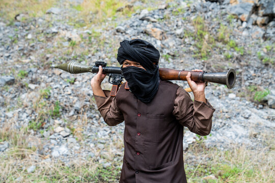 Man carries weapon on shoulder in rocky area during bright daylight hours