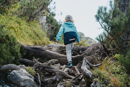 Cute little boy carefully climbing large rocks on steep mountain path. Happy safe childhood and active family nature travel.