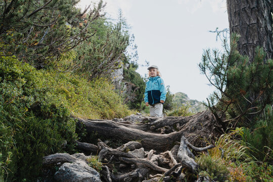 Cute little boy carefully climbing large rocks on steep mountain path. Happy safe childhood and active family nature travel.