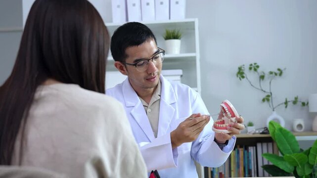 Asian male dentist holding a teeth model explaining oral care to a female doctor during a medical podcast interview. Recording a dental healthcare audio broadcast in a modern clinic studio.