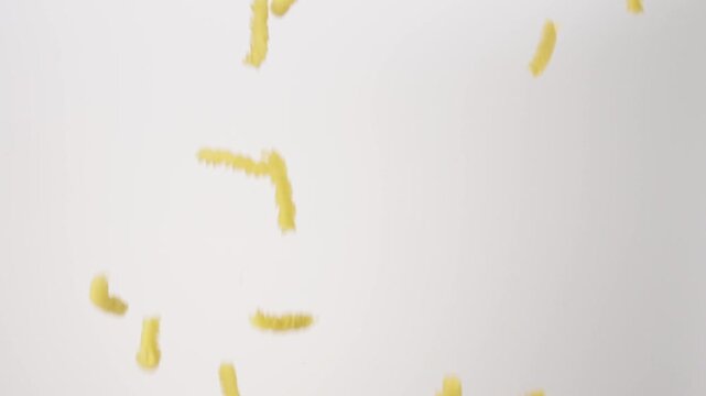 Raw fusilli pasta shapes falling down in slow motion against white background.