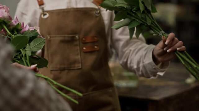 Female florist wearing apron cutting rose stems with pruners in wholesale warehouse. Footage is ideal for small business promotion or floristry school advertisements