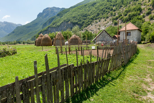 Vusanje, Gusinje Municipality, Montenegro - 28 July 2005: View of Vusanje with traditional haystacks, a rustic wooden fence, and stone houses nestled against the lush green mountains.