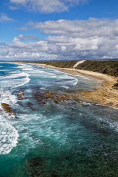 Vertical aerial view of the rugged headland and rocky coastline at Brooms Head with the long sandy shoreline of Sand Dune Beach, Pacific Ocean and surrounding natural coastal landscape 