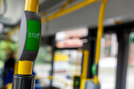 Green 'STOP' button inside a public transport bus, mounted on a yellow pole, for requesting a stop.