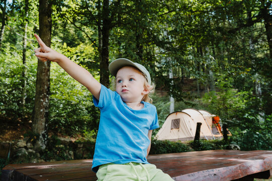 Curious boy sitting on a forest picnic table pointing his finger up towards the trees.