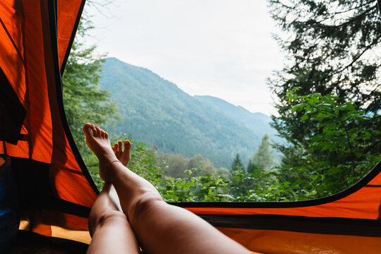 Bare feet resting inside an orange tent with a beautiful view of green mountain peaks.