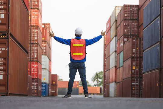 Worker in high visibility vest and hard hat standing between stacks of freight containers with shipping