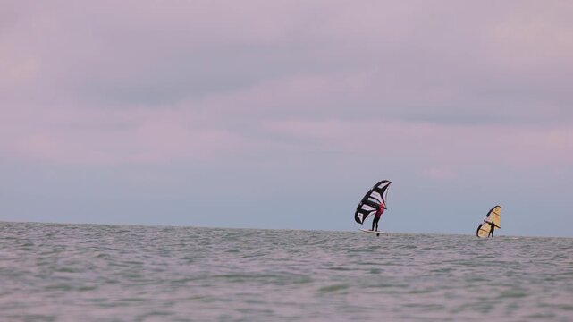 An athlete standing on the board holds on to the wing, in which the wind creates thrust in slow motion. Wingfoil board where a surfer glides through the water on a hydrofoil board.
