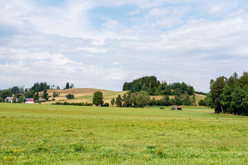Naklejka premium Expansive rural landscape featuring green fields, rolling hills, forests, and a distant village.
