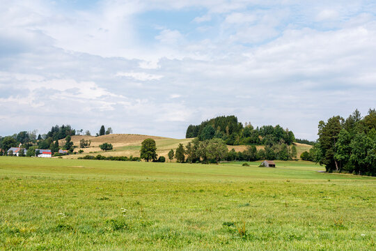 Expansive rural landscape featuring green fields, rolling hills, forests, and a distant village.