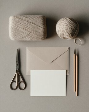 Minimalist flat lay of beige yarn, scissors, blank card, and envelope