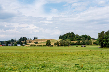 Naklejka premium Expansive rural landscape featuring green fields, rolling hills, scattered trees, and a distant vill