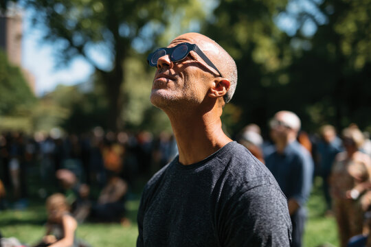 A man is gazing up at the sky, seemingly lost in thought during a sunny outdoor event, capturing a moment of reflection and appreciation for nature.