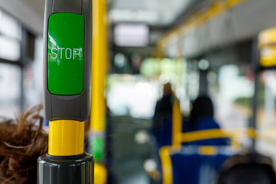 Close-up of a green stop request button inside a public bus with blurred passengers in the backgroun