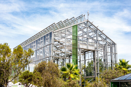 Large contemporary glass greenhouse structure for plants and horticulture under a bright blue sky.