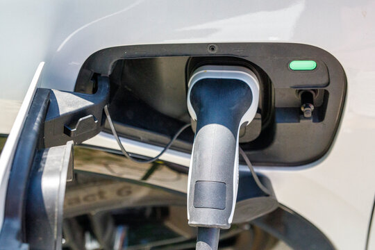 Electric vehicle charging cable plugged into a white car's port, symbolizing green energy.