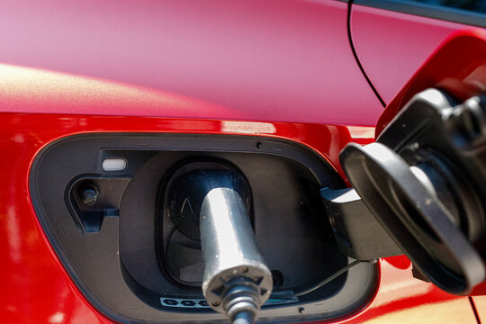 Close-up of an electric vehicle charging port with a cable plugged into a red car, symbolizing susta