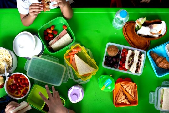 Children's hands reaching for colorful lunchboxes on a green table.