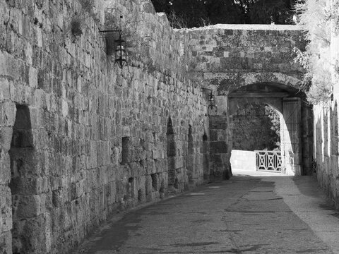 Historic stone fortress with a massive defensive wall, small embrasures, and a round-arched gateway in the medieval city of Rhodes