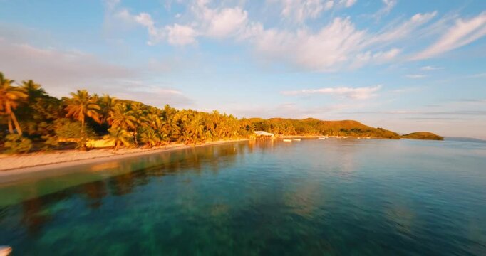 FPV aerial view of a wooden pier extending into the clear turquoise waters of a tropical coastline with a boat docked at the end during golden hour in Fiji.