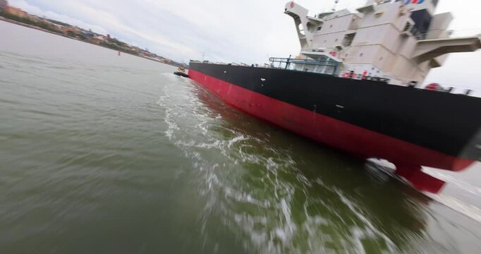 FPV aerial view of a large cargo ship being guided by a tugboat through the harbor waters in Newcastle, New South Wales, Australia.