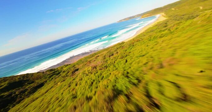 FPV aerial view of lush green forest canopy along the coastline with bright sunlight and ocean waves in Newcastle, New South Wales, Australia.