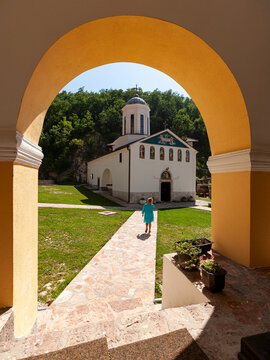 Pljevlja, Montenegro - 30 July 2005: View of Holy Trinity Monastery with a young girl walking along the stone path through the arched entrance.