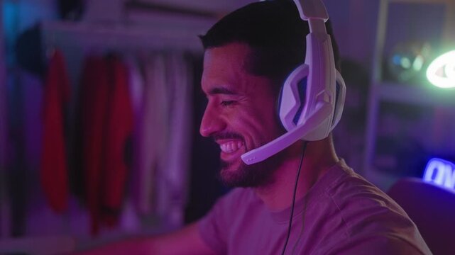 Man wearing a white headset smiling and leaning forward in a streaming studio while speaking into the headset microphone and facing a monitor; streaming joy.