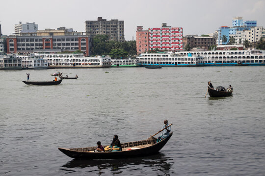 Dhaka, Bangladesh - 15 June 2026: View of Buriganga River with traditional wooden boats and commuters navigating the water against a backdrop of city buildings.