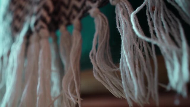Cream yarn tassels hanging from the edge of a woven textile, with loose strands, tied knots and a brown geometric pattern running along the fabric border above the fringe