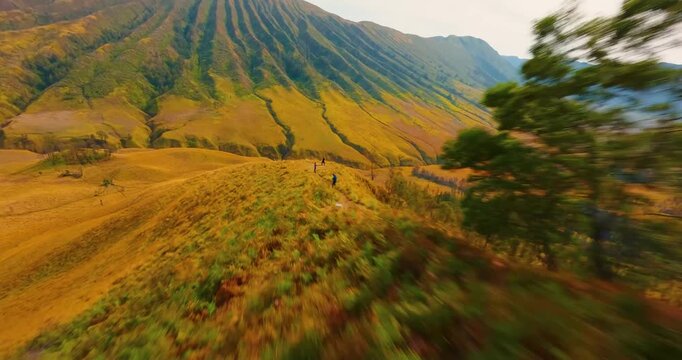 FPV aerial view of volcanic landscape with ridges and golden grasses in the Tengger Caldera, Indonesia.