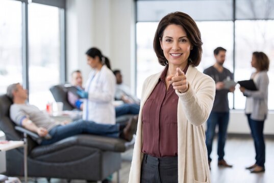 Smiling woman pointing to camera encouraging volunteer blood donors in a modern medical clinic