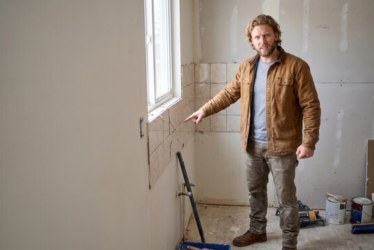 Man pointing at damaged wall tiles, expressing frustration with a diy home improvement project